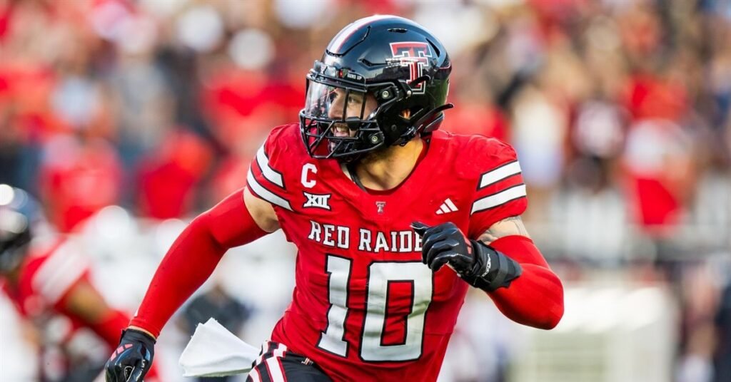 “A Texas Tech Red Raiders football player wearing a red jersey with the number 10, black helmet, and black gloves sprints across the field during a game. He appears focused and in motion, with a blurred crowd in the background.”