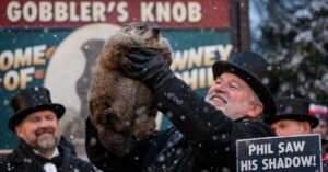 Punxsutawney Phil the groundhog is held aloft by his handler during the Groundhog Day ceremony in Punxsutawney, Pennsylvania, as snow falls and a sign announces his winter prediction.